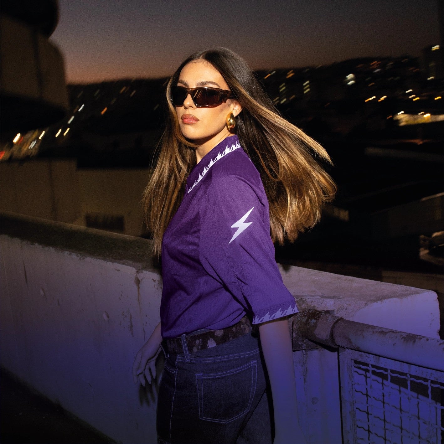 Sportlich gekleidete Person in Teamwear vor nächtlicher Stadtkulisse