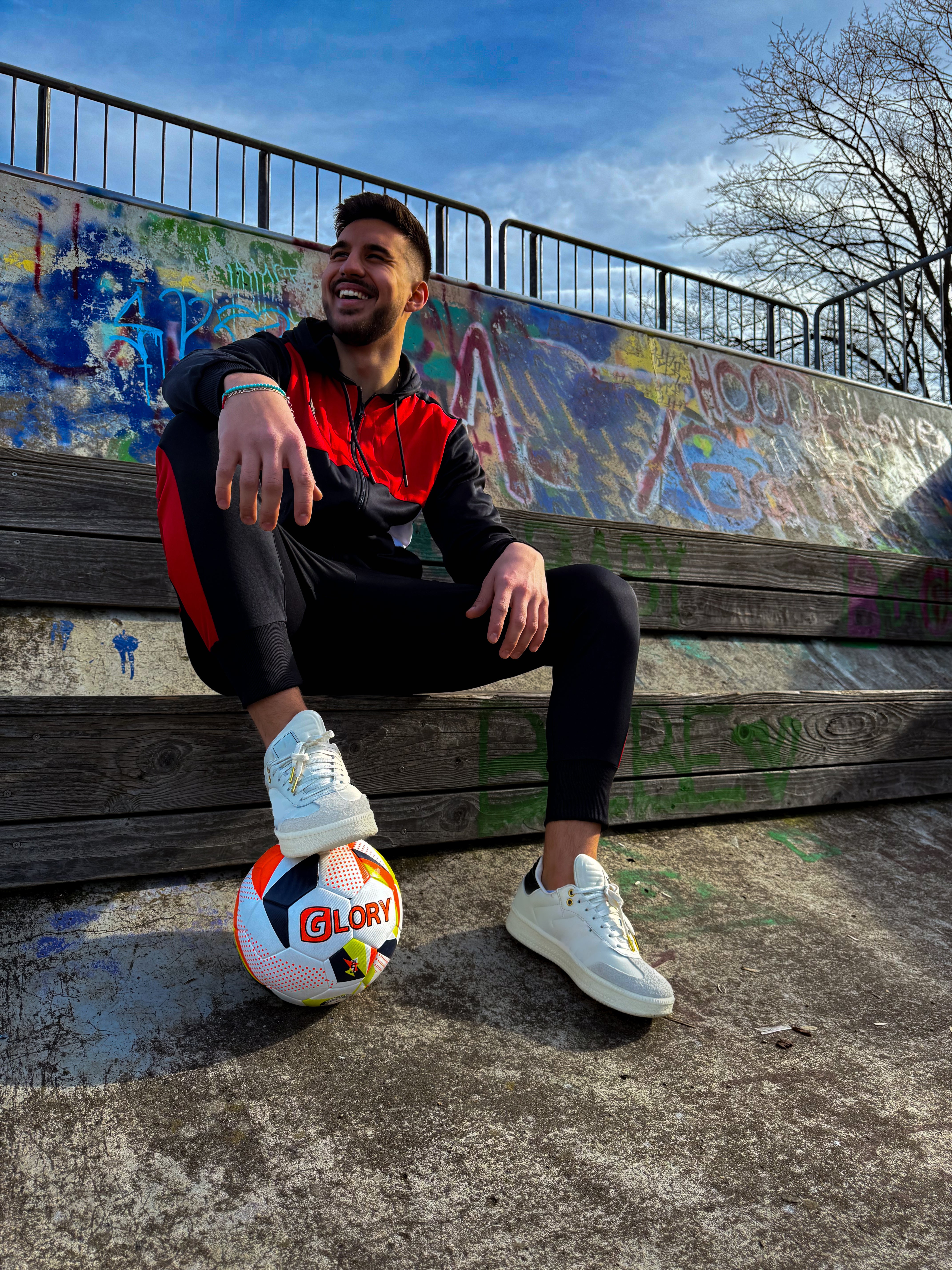 Sportler sitzt im Freien auf einer Treppe mit Fußball und Trainingsanzug