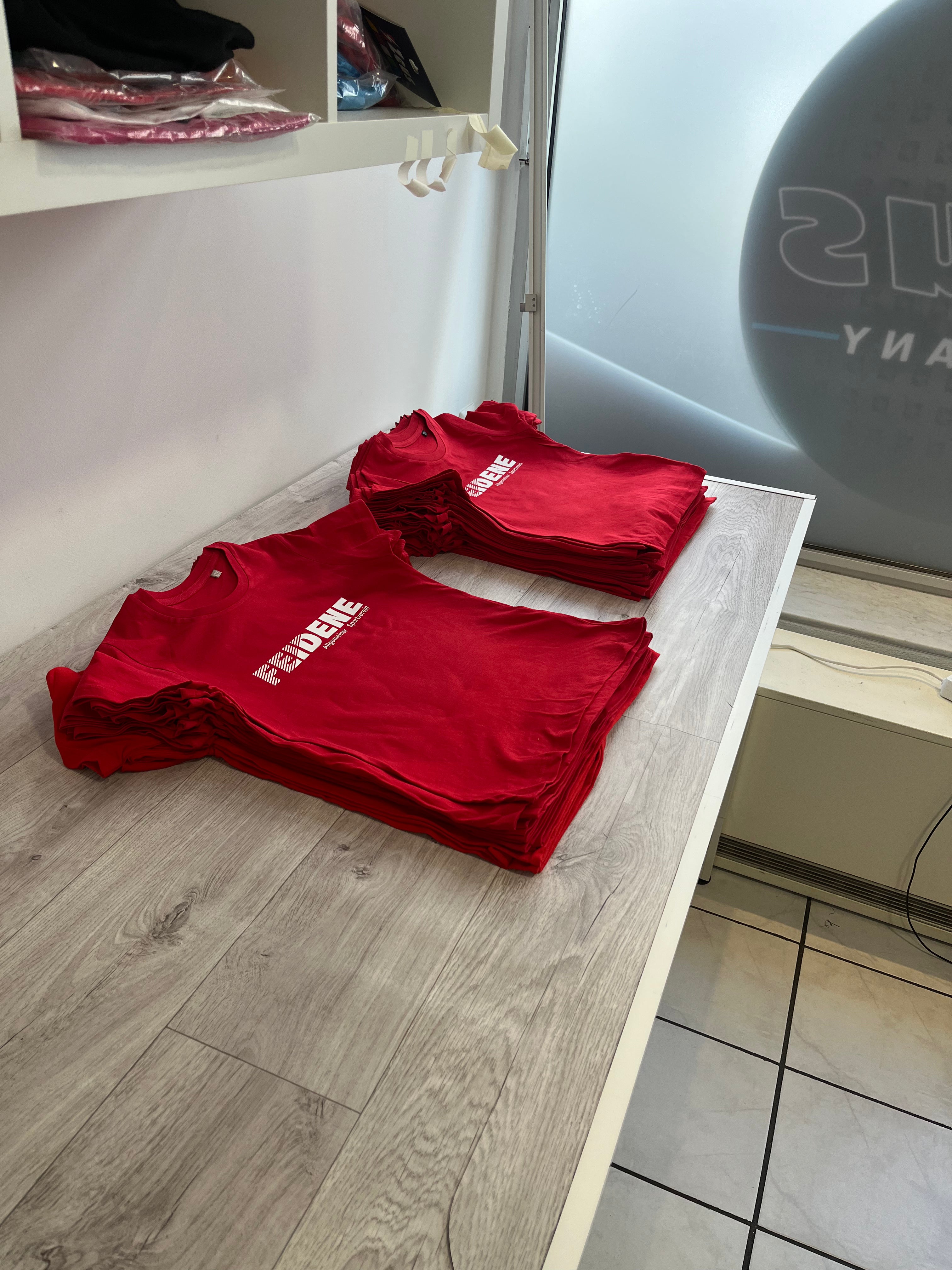 2 Stapel rote T-Shirts mit Aufdruck auf einem tisch